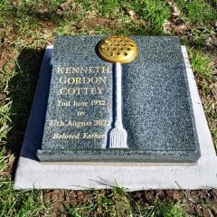 A gravestone by Memorial Masons for Kenneth Gordon Cottey (1932–2022), with gold lettering and a brass flower holder on top, set on grass with fallen leaves. The inscription reads: "Beloved Father.