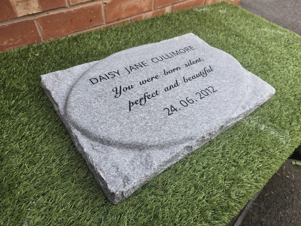 A small memorial stone on grass with the inscription: "Daisy Jane Cullimore. You were born silent, perfect and beautiful. 24.06.2012.