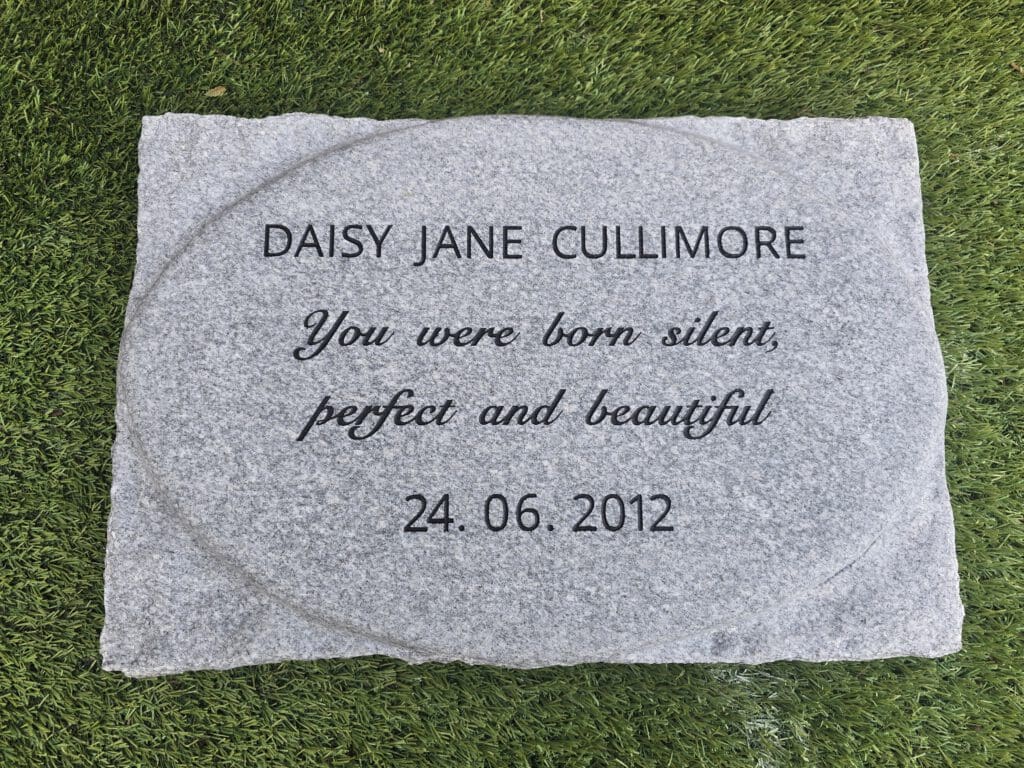 A memorial stone on grass engraved with "DAISY JANE CULLIMORE, You were born silent, perfect and beautiful, 24.06.2012.