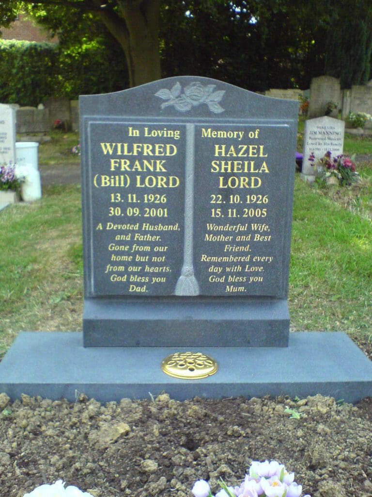 A double headstone in a cemetery. The left side is for Wilfred Frank Lord (Bill), 1926-2001, with an epitaph for a devoted husband and father. The right side is for Hazel Sheila Lord, 1926-2005, with an epitaph for a wonderful wife and best friend. Floral designs adorn the top.