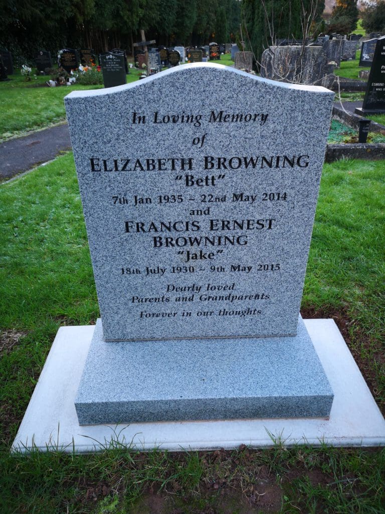 A gravestone in a cemetery is engraved with the names Elizabeth Browning and Francis Ernest Browning, along with their birth and death dates, surrounded by grass and other headstones in the background.