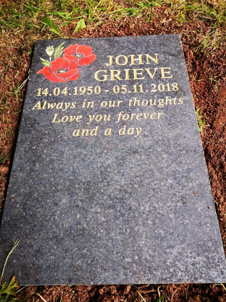 Gravestone with the name "John Grieve," dates "14.04.1950 - 05.11.2018," and the inscription "Always in our thoughts, Love you forever and a day." Red poppy flowers are etched above the name.