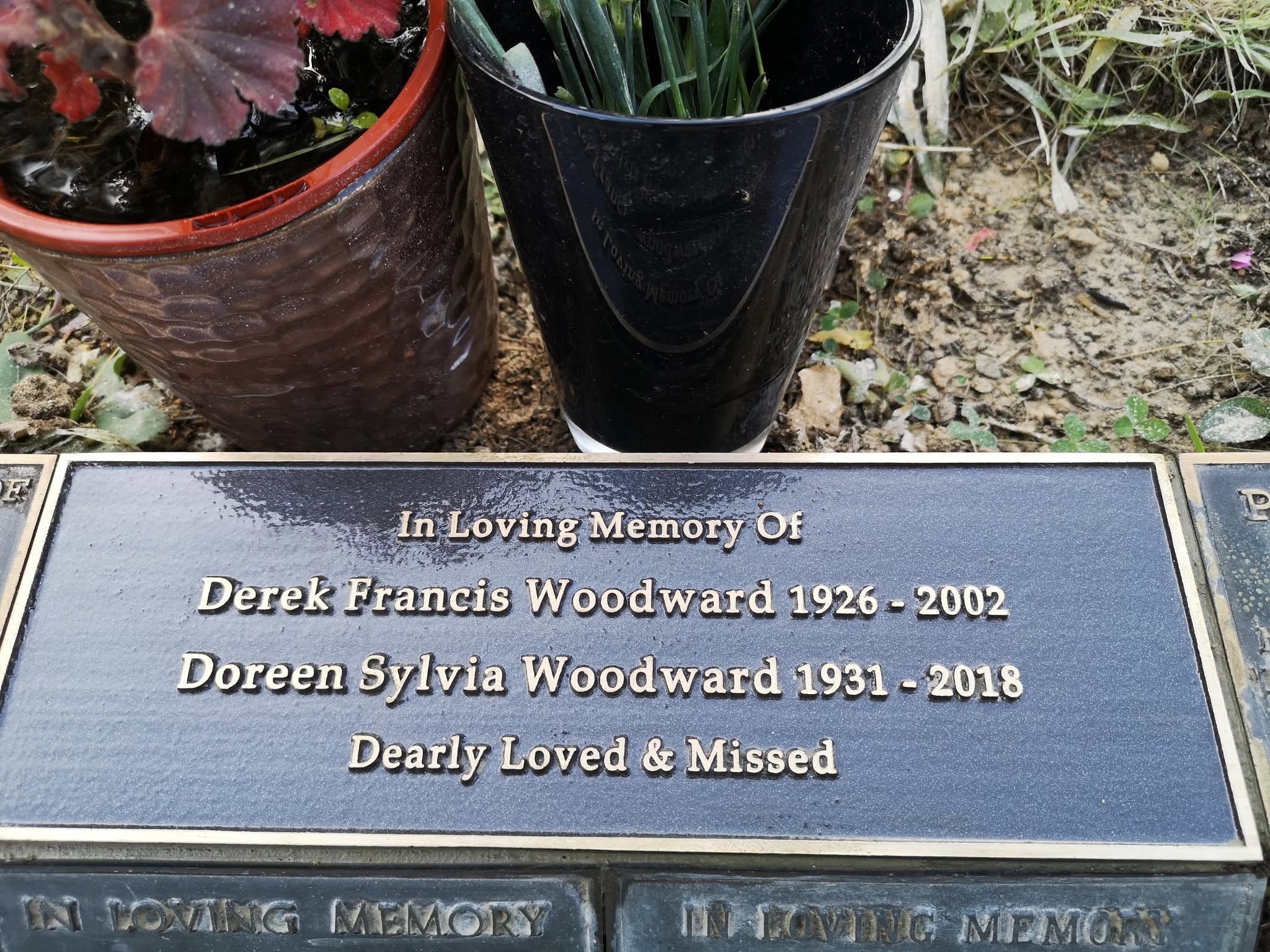 A memorial plaque for Derek Francis Woodward (1926–2002) and Doreen Sylvia Woodward (1931–2018), with flowers above and the inscription “Dearly Loved & Missed.”.