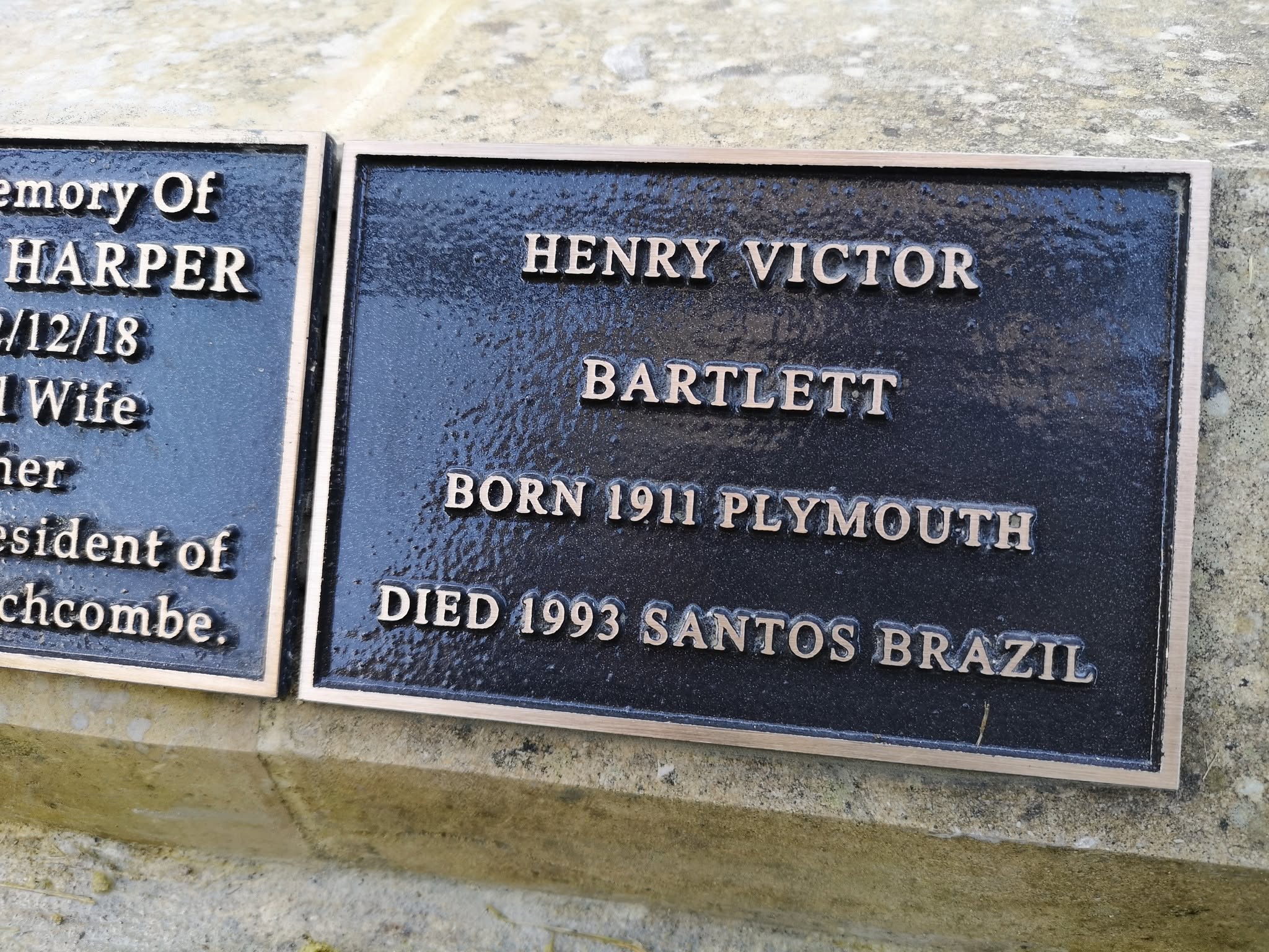 A bronze memorial plaque for Henry Victor Bartlett, born 1911 in Plymouth, died 1993 in Santos, Brazil, mounted on a stone surface next to another partially visible plaque.