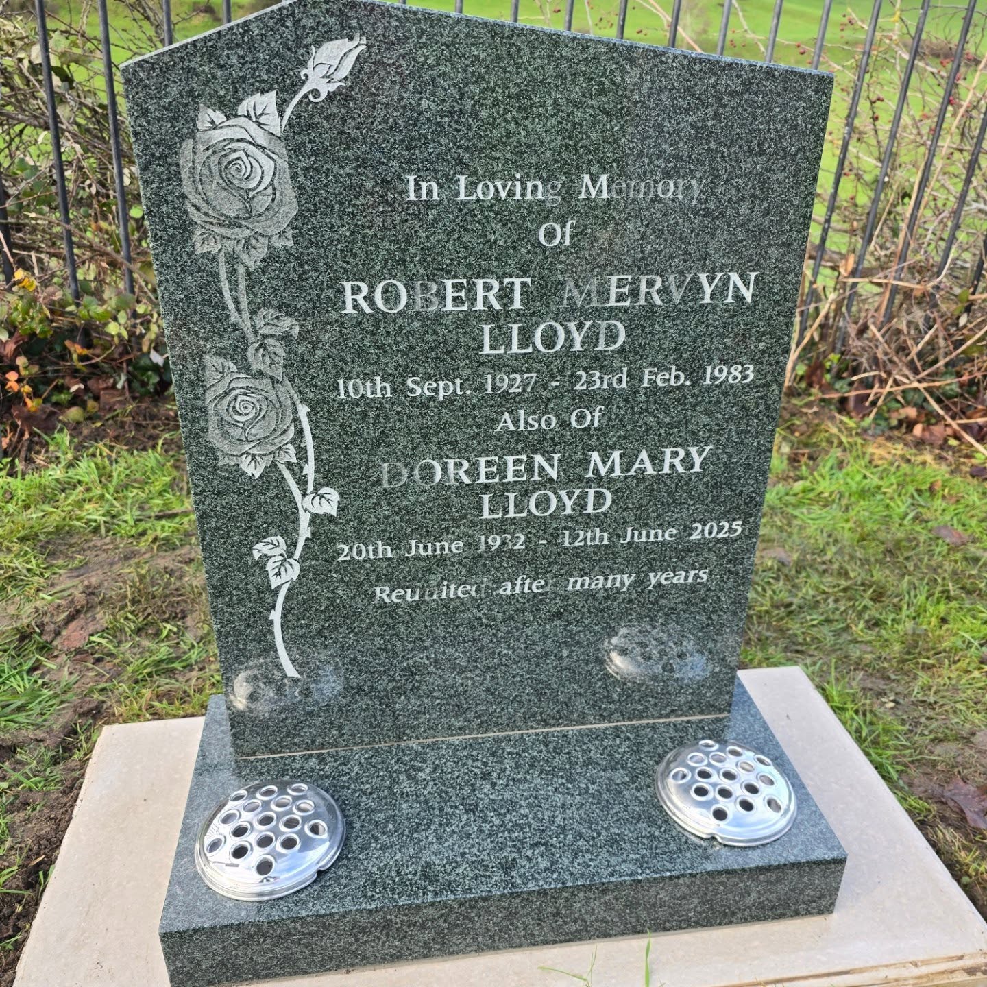 A polished granite headstone with rose carvings commemorates Robert Mervyn Lloyd (1927–1983) and Doreen Mary Lloyd (1932–2023). The inscription notes they are reunited after many years.